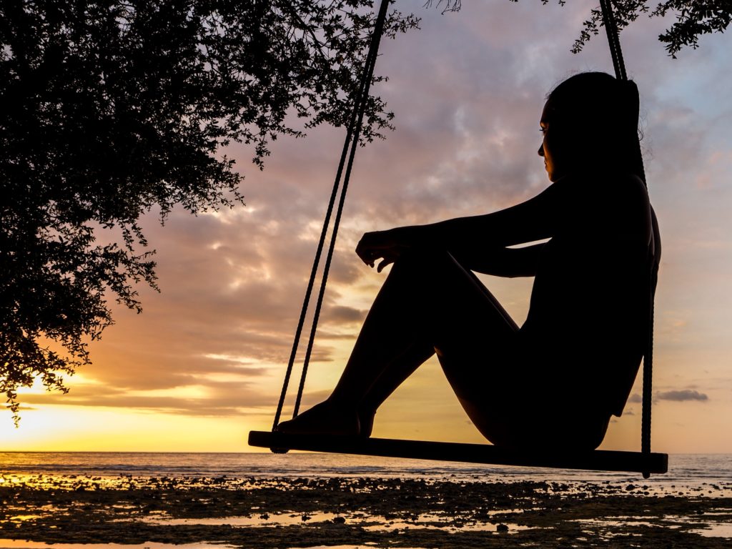 Silhouette of person on a wooden swing by the ocean. Rediscovering yourself after trauma.
