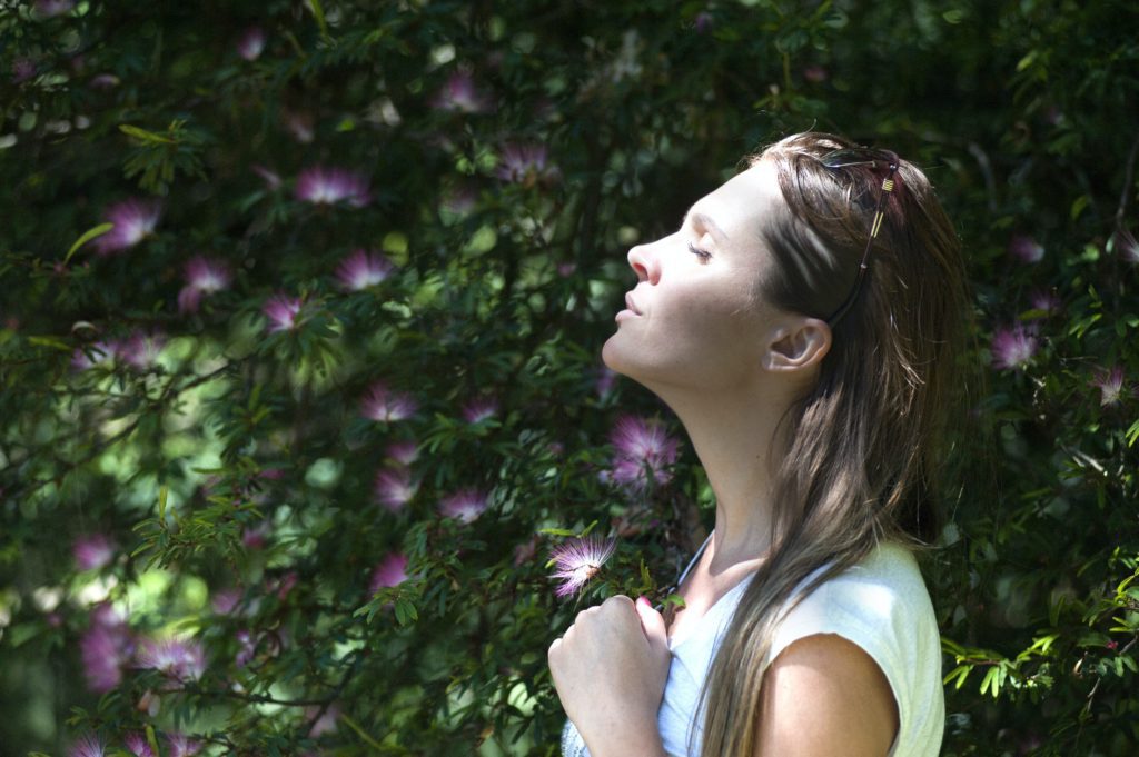 Woman deep breathing outside in a green space. Healing through therapy.
