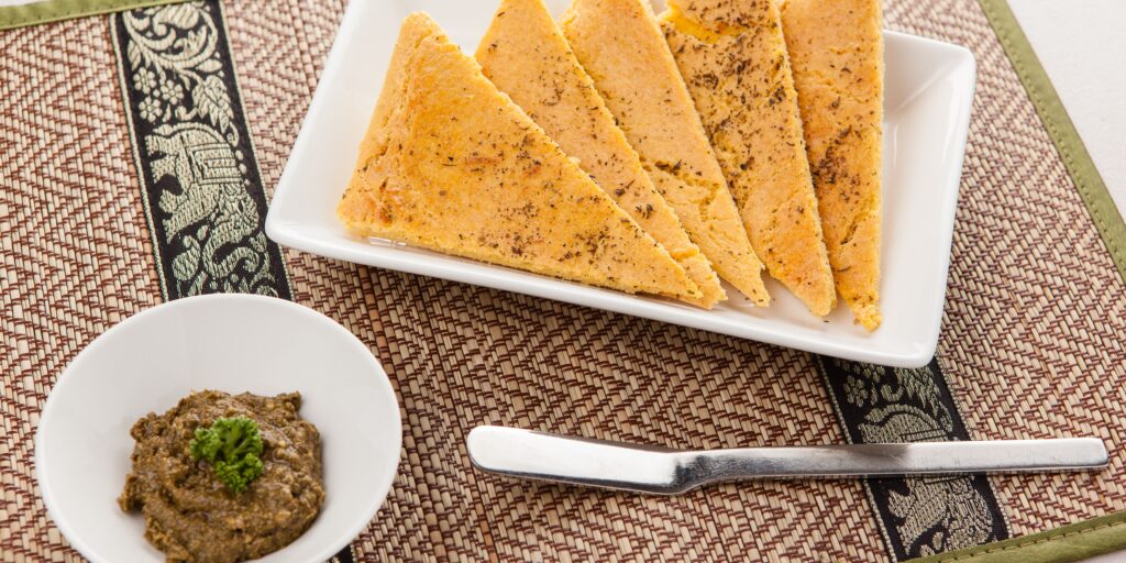 Flatbread slices on a white ceramic plate with dip in a ramakin on the left side on a wood table background. How to eat beans and grains on a lectin-free diet. 